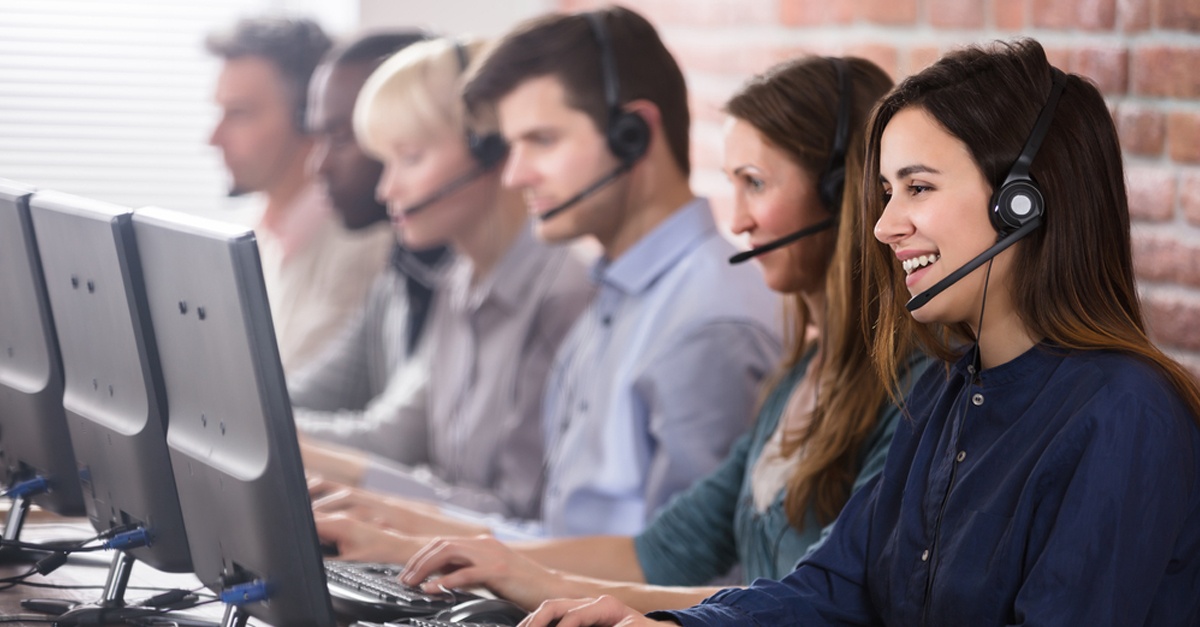 Row of workers talking on the phone with headsets, in front of their computers