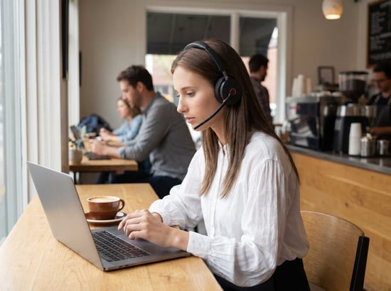 Woman wearing a Yealink WH68 headset at a coffee shop -- distributed by TeleDynamics