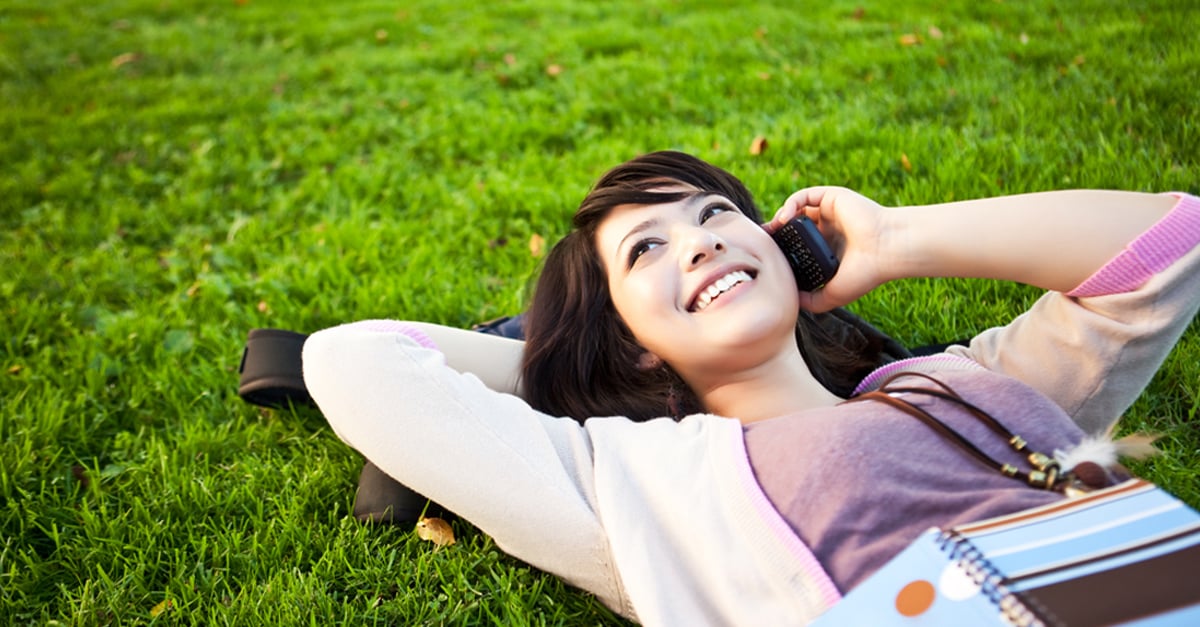Smiling woman lying on a lawn, talking on the phone